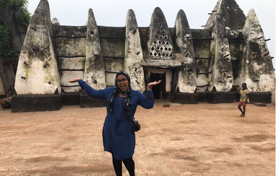 smiling woman with their hands up in front of a Ghanies historical building