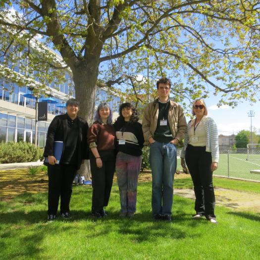 Four student stand shoulder to shoulder infront of tree on a sunny day