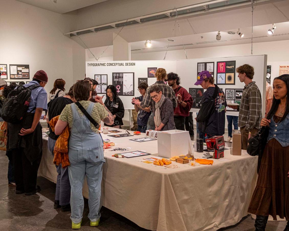 Photo of part of the Design exhibition, showing students mingling at the opening reception.