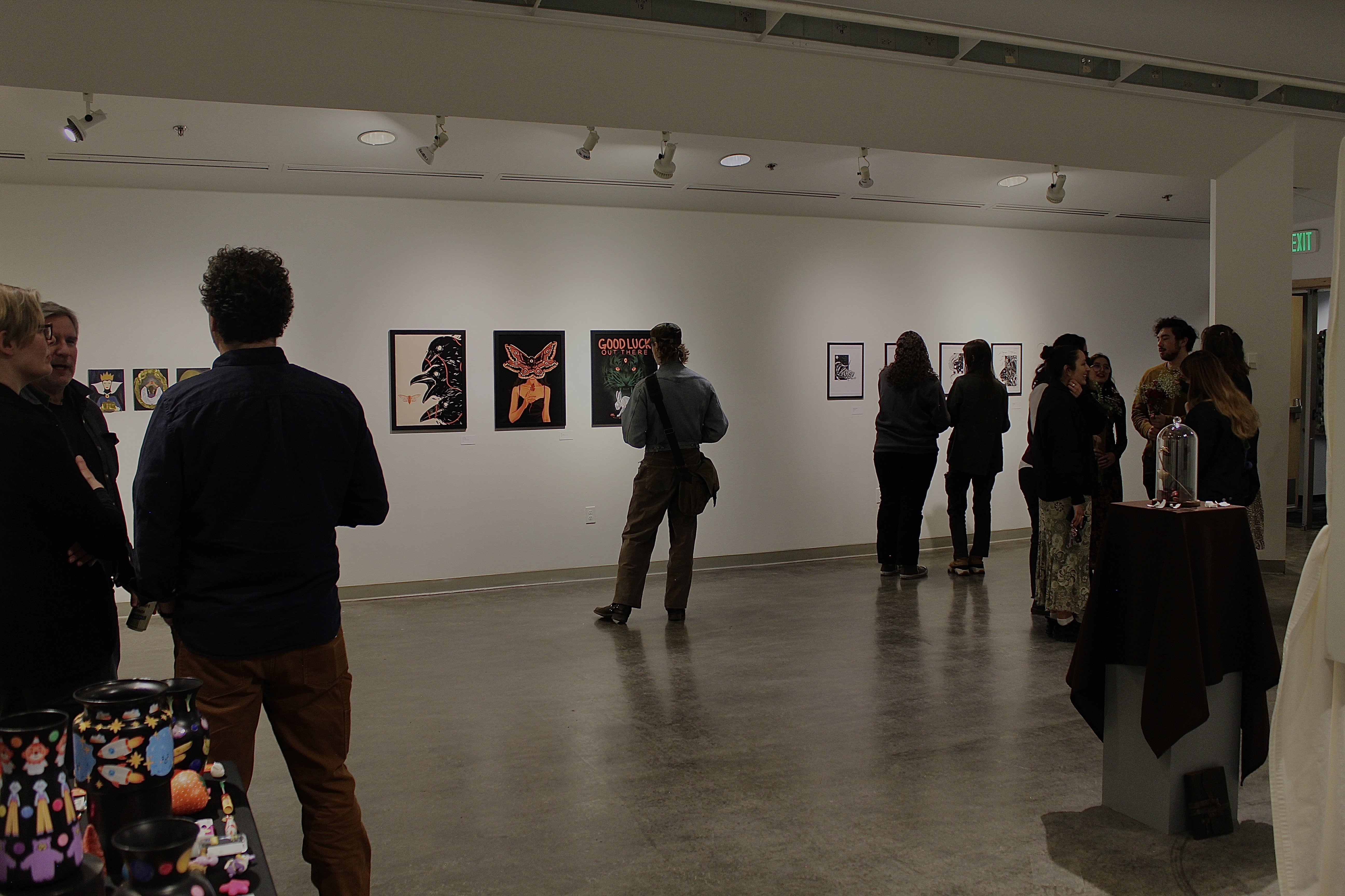 Gallery with visual art on the wall, 3D on a table and people walking around