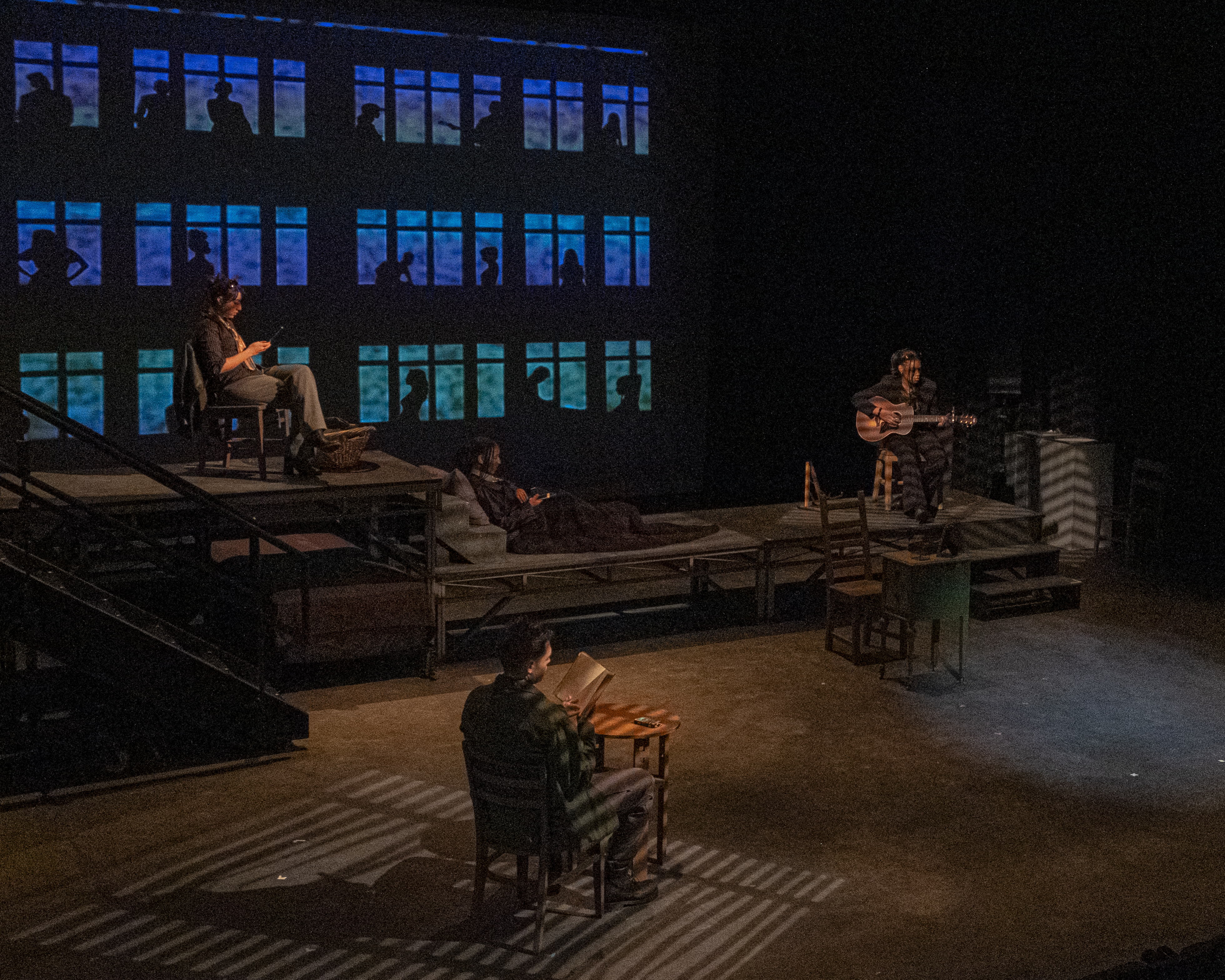 Dark theater with multiple actors placed about reading or playing music