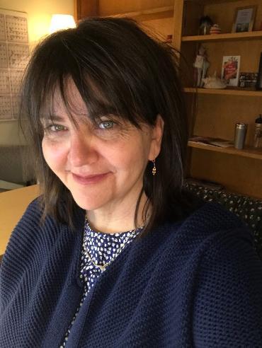 A woman in a blue cardigan smiles in front of a desk.
